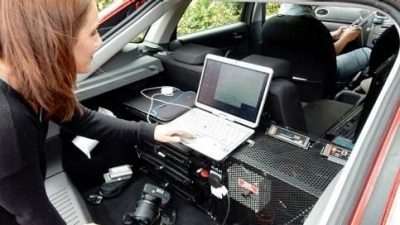 A student working on a lap top in the back open section of a car with various electronics.