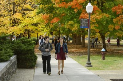 Students walking down a sidewalk on campus in the autumn.