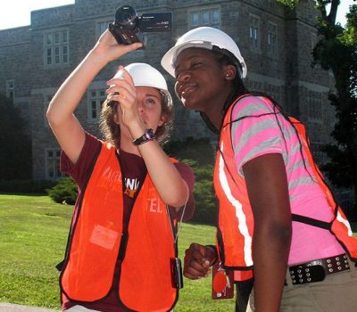 Two girls from the CTech2 program in protective vests and hardhats using videocamera